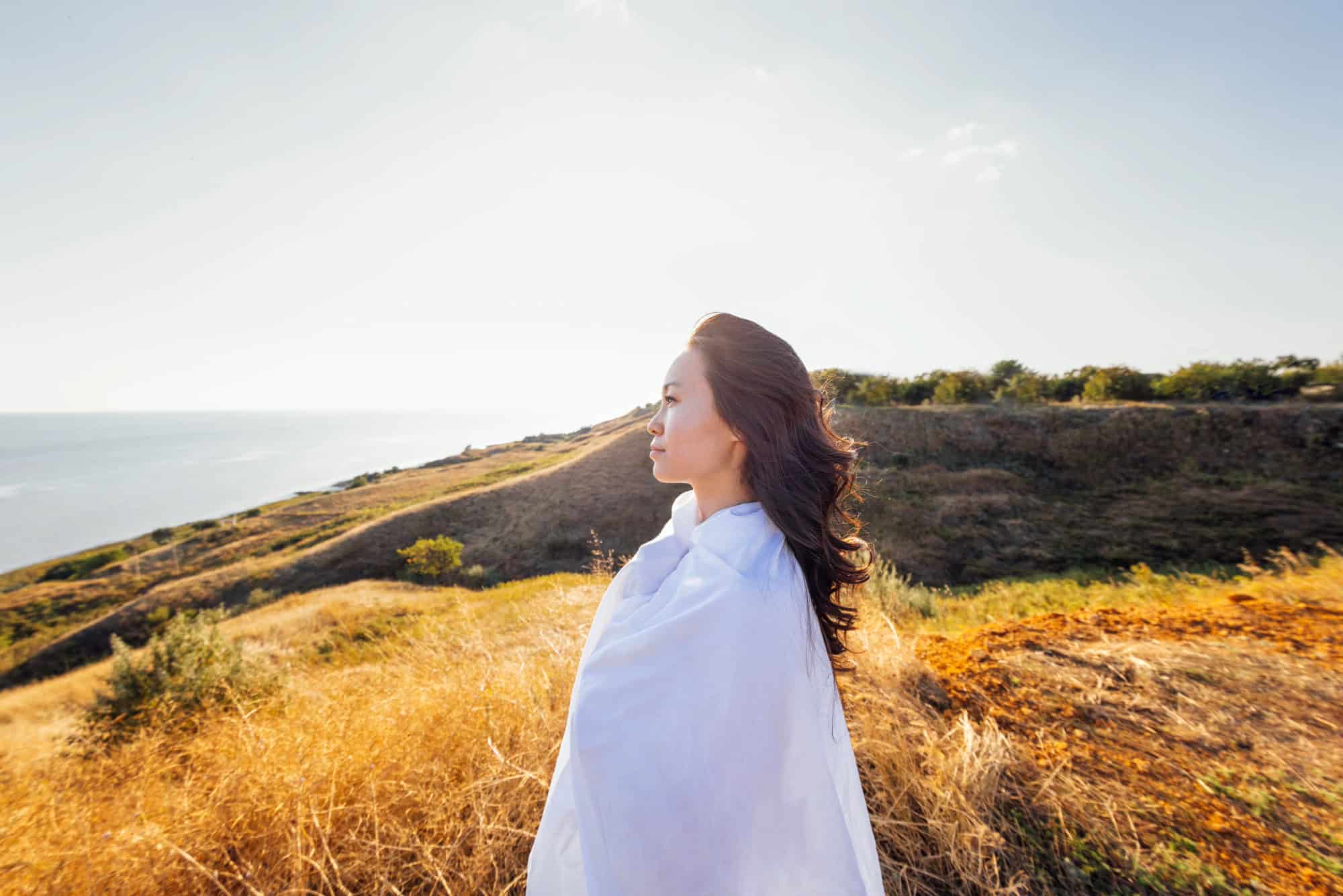 Serene woman wrapped in white, breathing deeply in nature, symbolizing cellular renewal and inner balance.