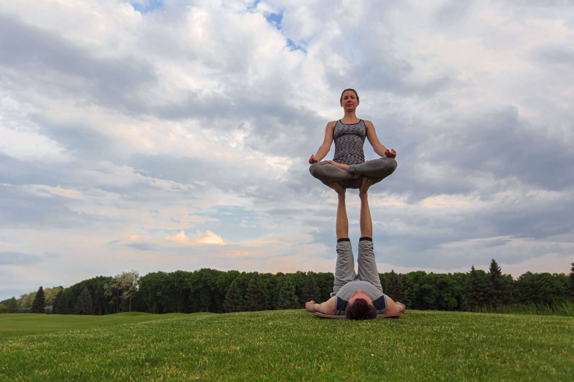 Man and woman performing a balancing yoga pose outdoors, symbolising Ascleus’s holistic approach to energy alignment and body balance.