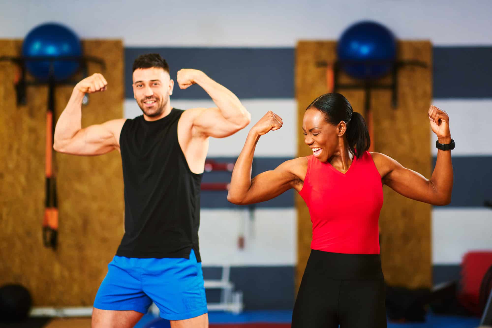 Fit man and woman flexing muscles and smiling in a gym, symbolising Ascleus therapy for energy, strength and recovery.